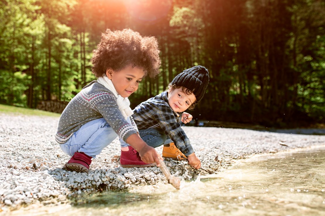 Zwei Kinder spielen am kiesbedeckten Ufer eines Alpensees. Two kids playing at the gravelly beach of a tarn.