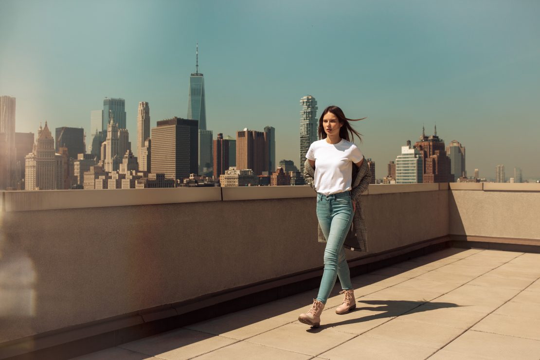 Woman in a white top and jeans on a rooftop overlooking the Manhattan skyline for Deichmann.