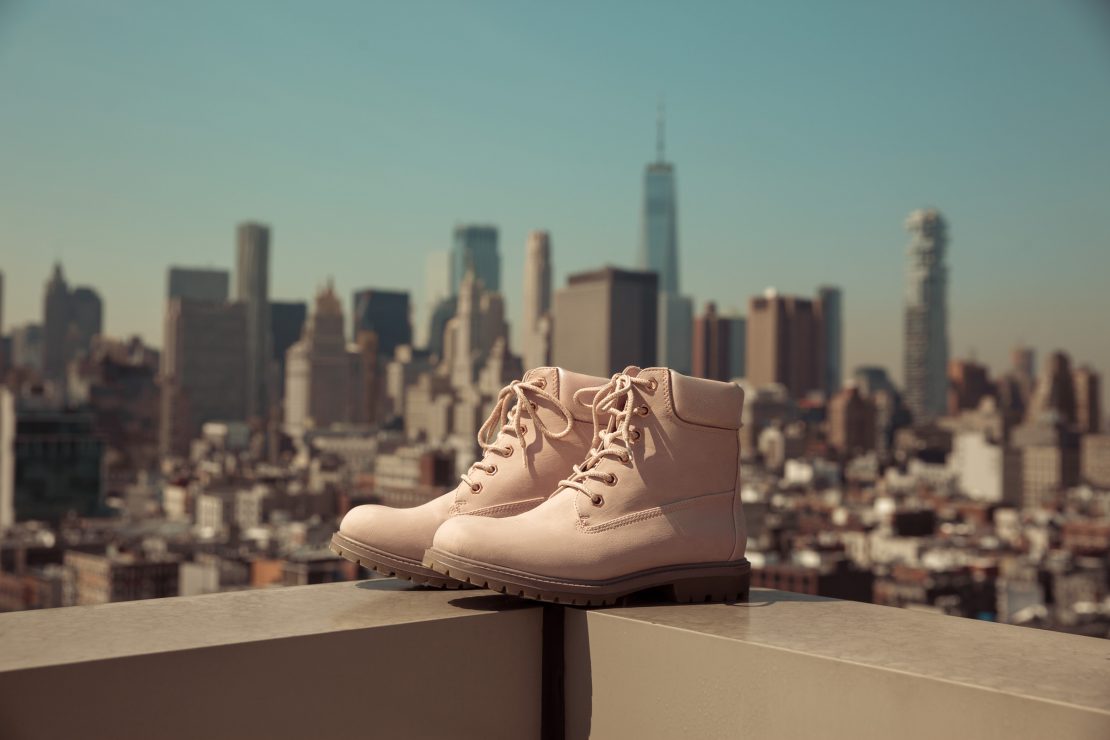 Pale pink lace-up boots displayed on a rooftop ledge with the Manhattan skyline behind them.