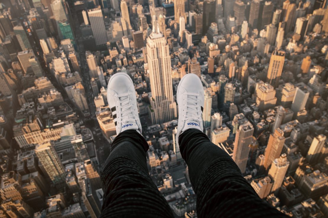 White trainers and outstretched legs above the skyscrapers of Manhattan, photographed from a helicopter.